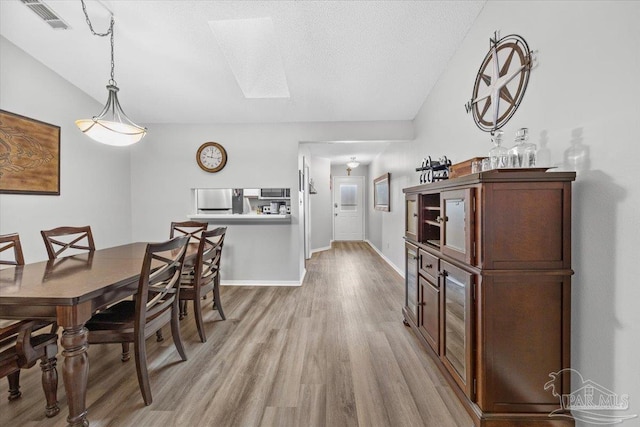 dining room with a textured ceiling, light hardwood / wood-style flooring, and vaulted ceiling with skylight