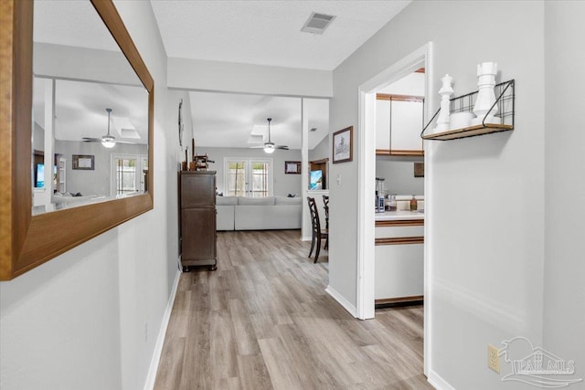 hallway with a textured ceiling, light wood-type flooring, vaulted ceiling, and french doors