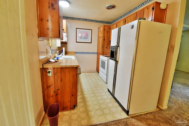 kitchen featuring white appliances, light carpet, a textured ceiling, and sink