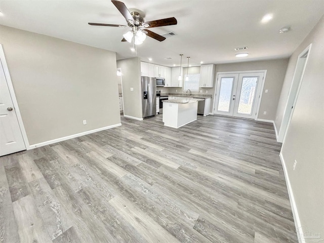 unfurnished living room with ceiling fan, light wood-style flooring, a sink, visible vents, and baseboards