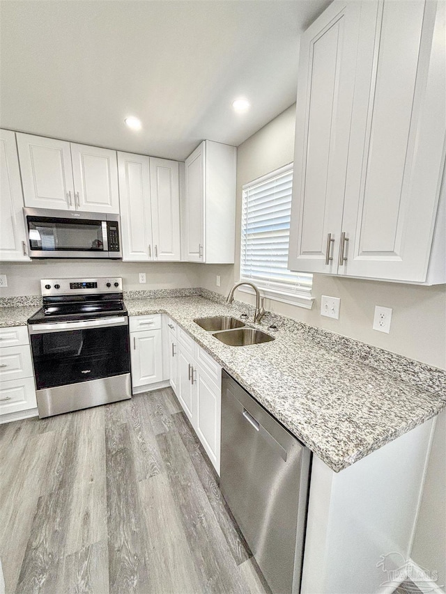 kitchen featuring appliances with stainless steel finishes, light wood-type flooring, white cabinetry, and a sink