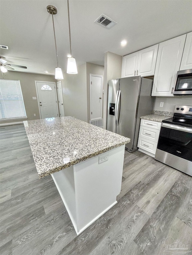 kitchen featuring white cabinets, a kitchen island, stainless steel appliances, and hanging light fixtures