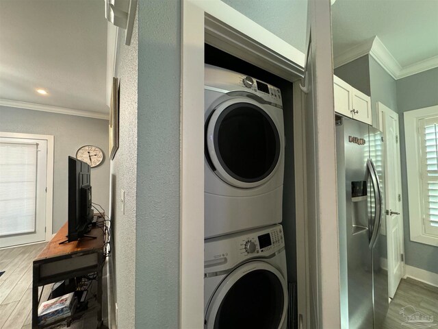 laundry area with hardwood / wood-style flooring, crown molding, and stacked washer and clothes dryer