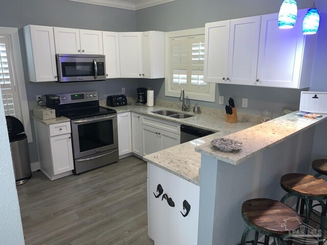 kitchen featuring hanging light fixtures, hardwood / wood-style floors, a breakfast bar area, white cabinets, and appliances with stainless steel finishes