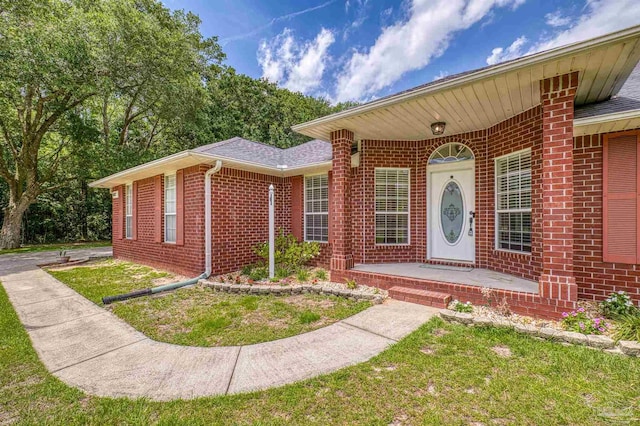 doorway to property featuring brick siding and a lawn
