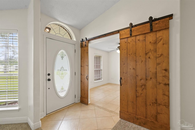 foyer entrance featuring a barn door, light tile patterned floors, healthy amount of natural light, baseboards, and vaulted ceiling
