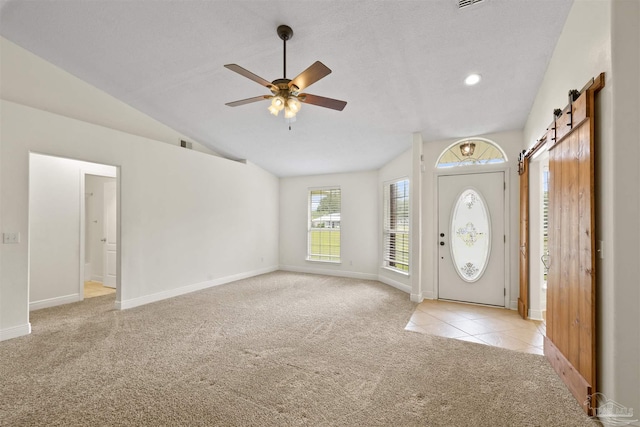 tiled foyer with carpet flooring, a ceiling fan, baseboards, lofted ceiling, and a barn door