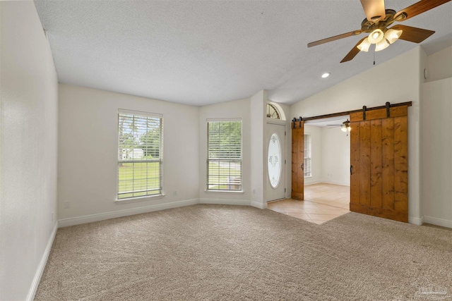 spare room featuring a barn door, ceiling fan, light colored carpet, a textured ceiling, and vaulted ceiling