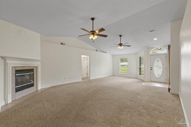 unfurnished living room featuring ceiling fan, light carpet, vaulted ceiling, a tiled fireplace, and baseboards