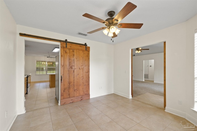 spare room with a barn door, light tile patterned floors, ceiling fan, and baseboards