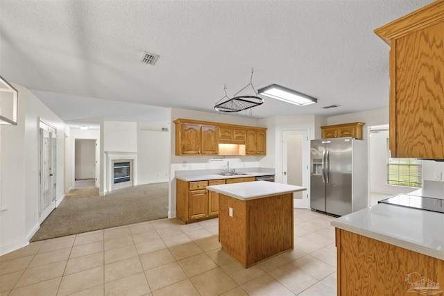 kitchen with stainless steel fridge with ice dispenser, a kitchen island, a sink, light countertops, and a textured ceiling