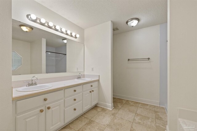 full bath with double vanity, baseboards, a textured ceiling, and a shower