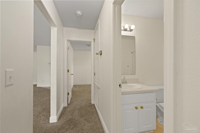 hallway with a sink, light carpet, a textured ceiling, and baseboards