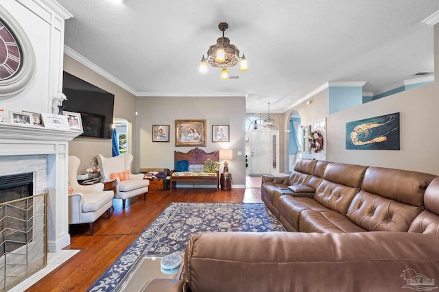 living room featuring a textured ceiling, a chandelier, a tile fireplace, crown molding, and dark hardwood / wood-style flooring