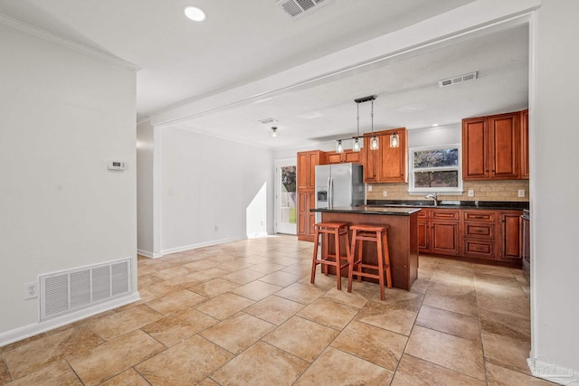 kitchen with dark countertops, visible vents, backsplash, a sink, and stainless steel fridge