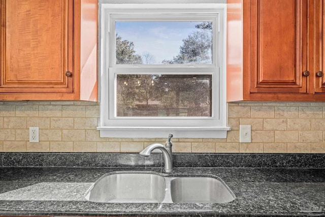 kitchen featuring dark stone counters, tasteful backsplash, a sink, and brown cabinets