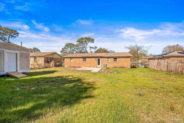 back of house featuring an outbuilding, brick siding, fence, a yard, and a storage unit