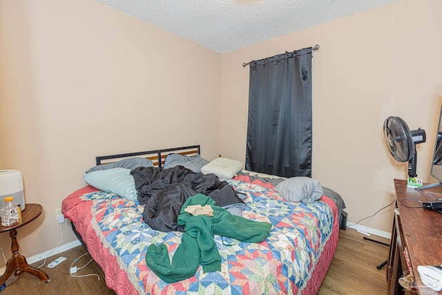 bedroom with a textured ceiling, baseboards, and wood finished floors