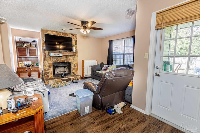 living area featuring visible vents, a textured ceiling, a stone fireplace, and a ceiling fan