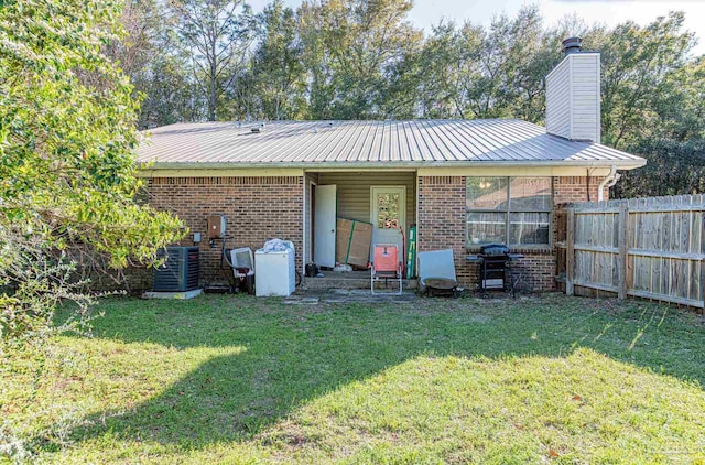 rear view of house featuring brick siding, metal roof, a yard, and fence