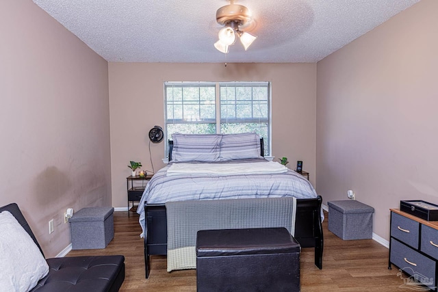 bedroom featuring ceiling fan, baseboards, a textured ceiling, and wood finished floors