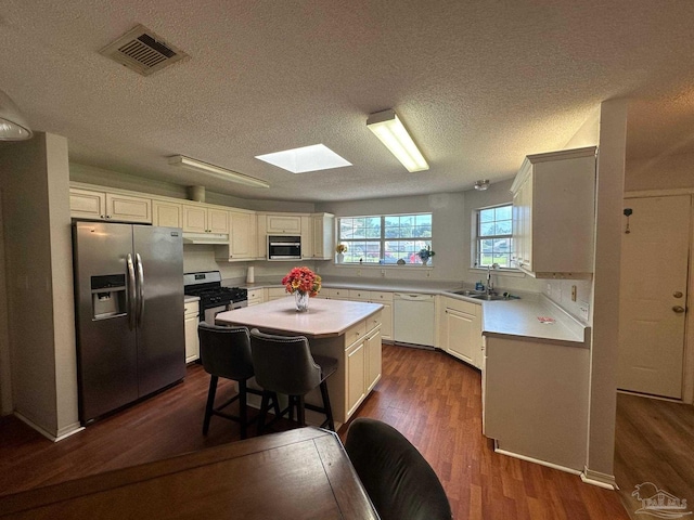 kitchen featuring stainless steel appliances, sink, a textured ceiling, a kitchen island, and dark wood-type flooring