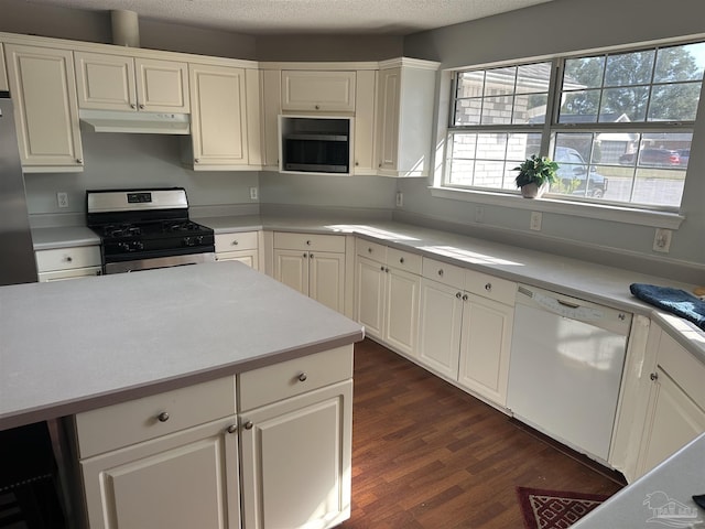 kitchen featuring built in microwave, under cabinet range hood, gas range, white dishwasher, and a textured ceiling