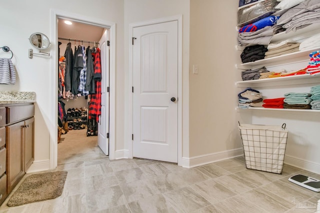 interior space with a walk in closet, vanity, and baseboards