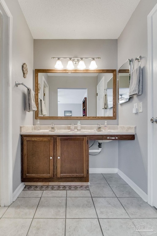 bathroom featuring a textured ceiling, a sink, tile patterned flooring, and baseboards