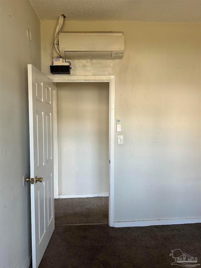 hallway featuring a wall mounted air conditioner, carpet flooring, and a textured ceiling