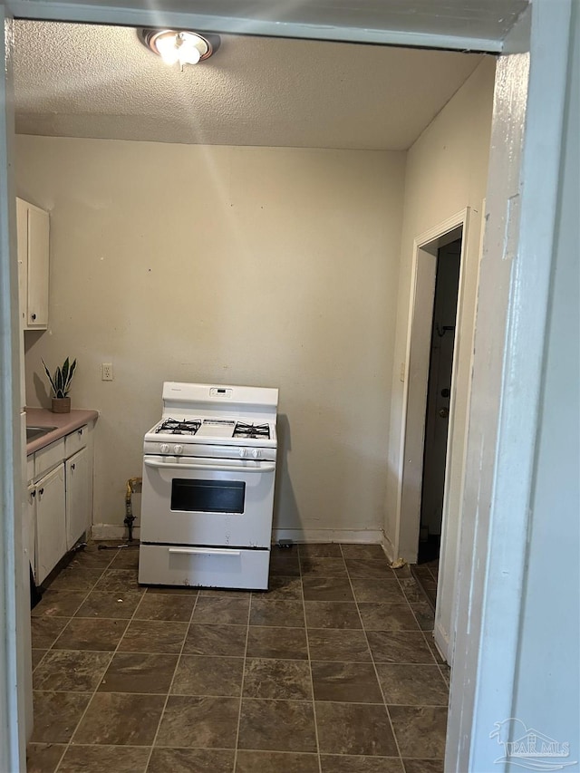 kitchen with a textured ceiling, white gas range oven, and white cabinets