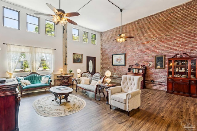 living room featuring hardwood / wood-style flooring, brick wall, a healthy amount of sunlight, and a towering ceiling