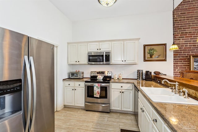 kitchen with pendant lighting, sink, appliances with stainless steel finishes, white cabinetry, and stone countertops