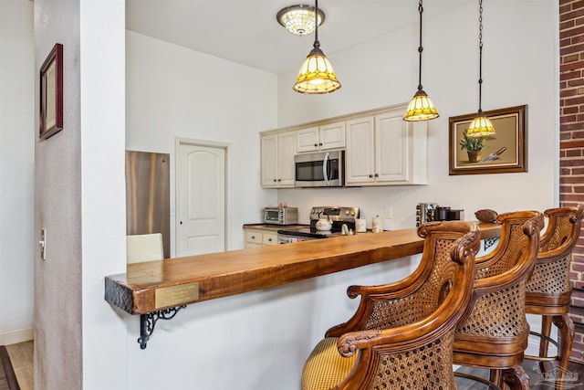 kitchen with pendant lighting, butcher block countertops, a kitchen bar, stainless steel appliances, and cream cabinets