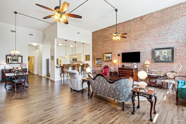 living room with hardwood / wood-style floors, a towering ceiling, ceiling fan, and brick wall