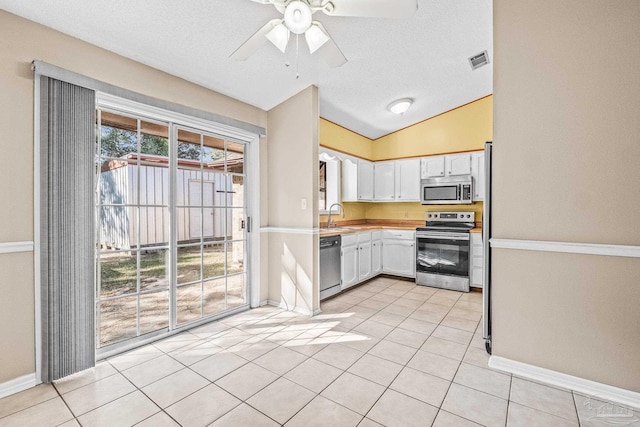 kitchen with white cabinetry, sink, stainless steel appliances, vaulted ceiling, and light tile patterned floors