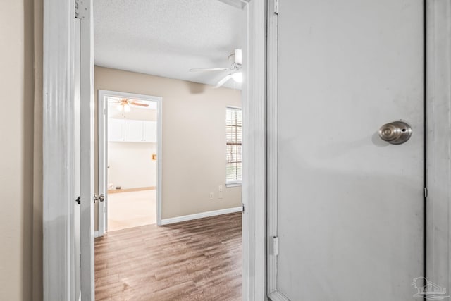 corridor with light wood-type flooring and a textured ceiling