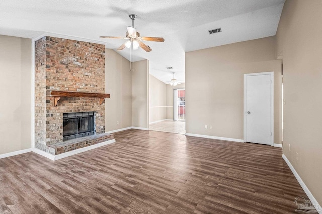 unfurnished living room featuring ceiling fan, a brick fireplace, hardwood / wood-style floors, a textured ceiling, and lofted ceiling