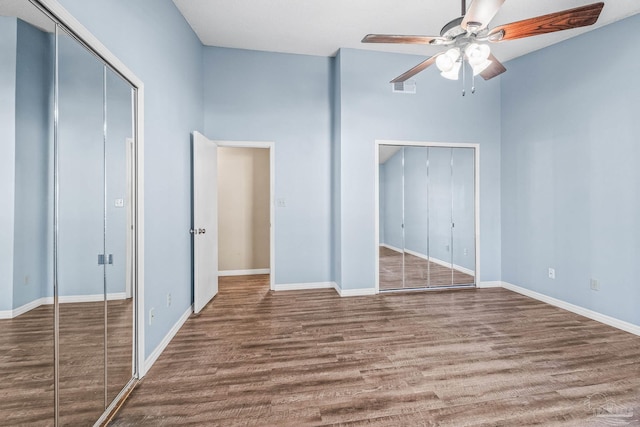 unfurnished bedroom with hardwood / wood-style floors, ceiling fan, and two closets