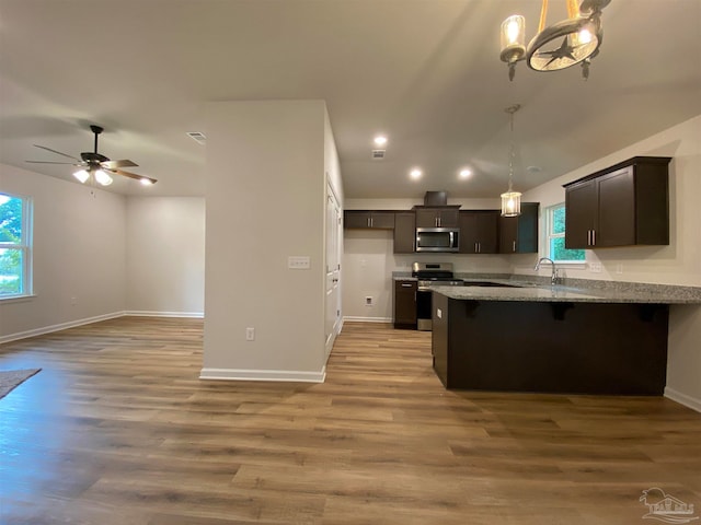 kitchen featuring stainless steel appliances, light wood-type flooring, decorative light fixtures, dark brown cabinetry, and sink