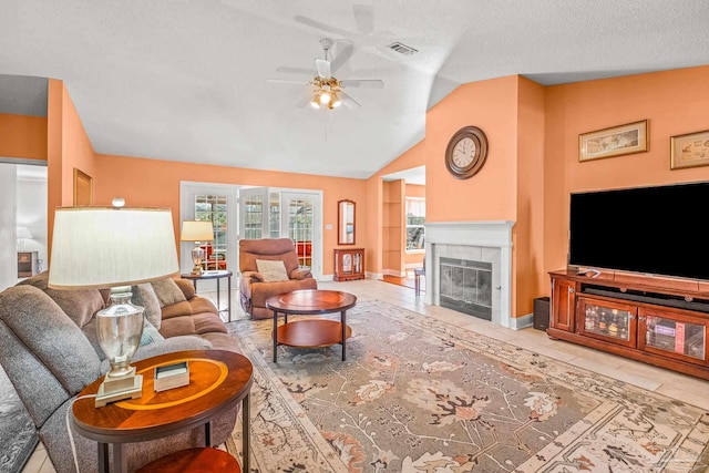 tiled living room with a textured ceiling, vaulted ceiling, ceiling fan, and a tiled fireplace