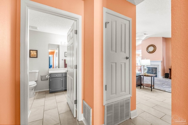 corridor featuring vaulted ceiling, light tile patterned flooring, and a textured ceiling