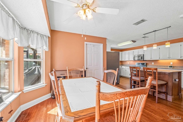 dining space with rail lighting, ceiling fan, a textured ceiling, and light hardwood / wood-style flooring