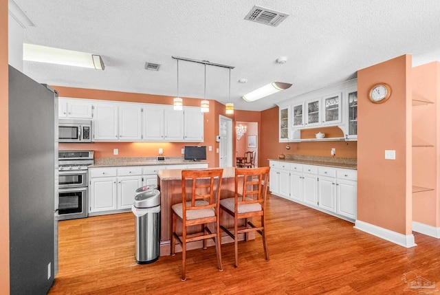 kitchen with pendant lighting, white cabinetry, stainless steel appliances, and light hardwood / wood-style flooring