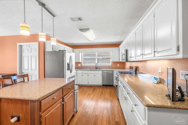 kitchen with track lighting, white cabinets, hanging light fixtures, light hardwood / wood-style flooring, and stainless steel appliances