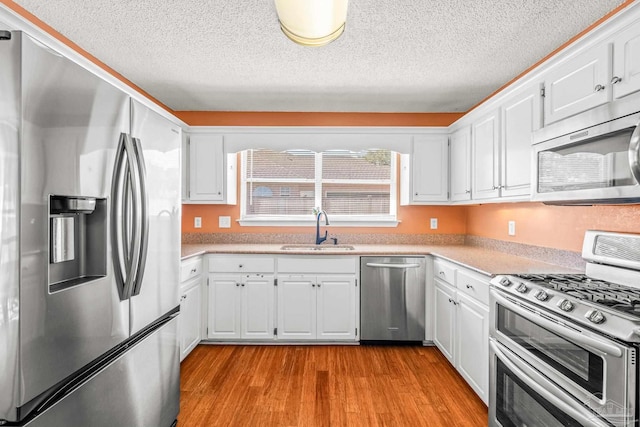 kitchen with sink, stainless steel appliances, a textured ceiling, white cabinets, and light wood-type flooring