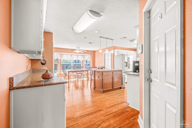 kitchen featuring ceiling fan, light wood-type flooring, decorative light fixtures, a kitchen island, and stainless steel fridge with ice dispenser