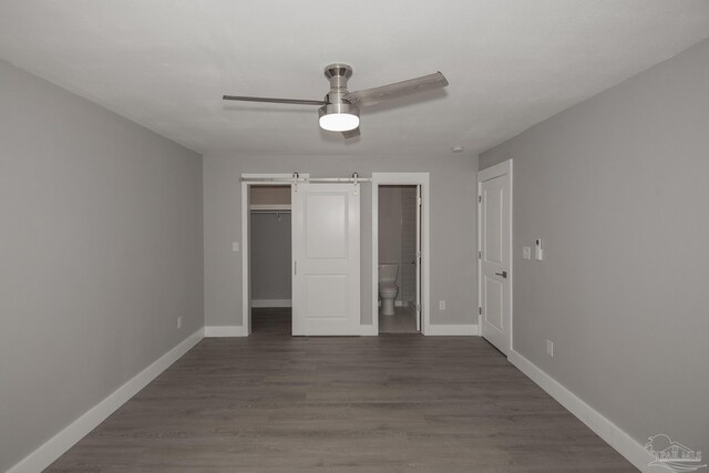 unfurnished bedroom featuring ceiling fan, a barn door, ensuite bathroom, and dark hardwood / wood-style floors