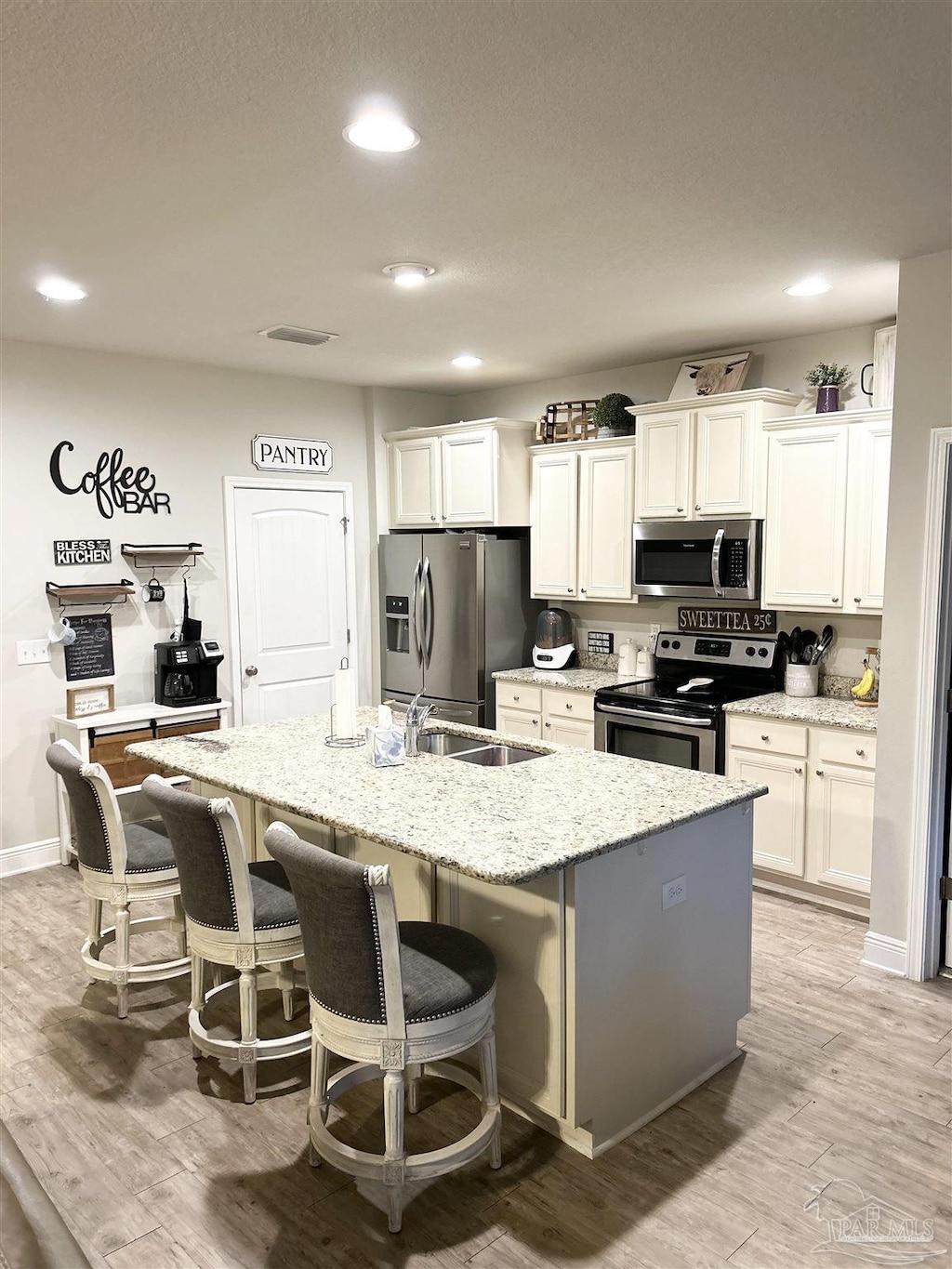 kitchen featuring light wood finished floors, a kitchen breakfast bar, white cabinets, stainless steel appliances, and a kitchen island with sink