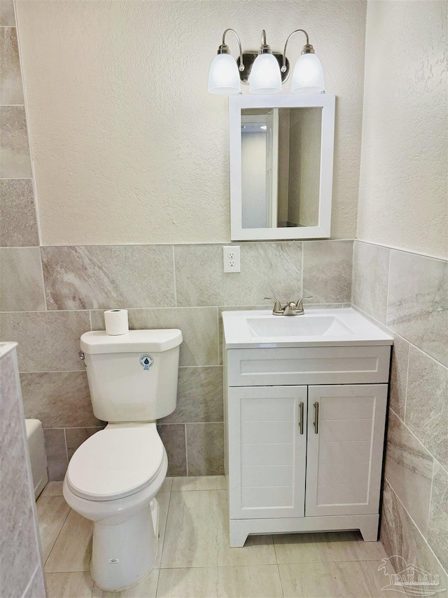 bathroom with vanity, tile walls, and toilet